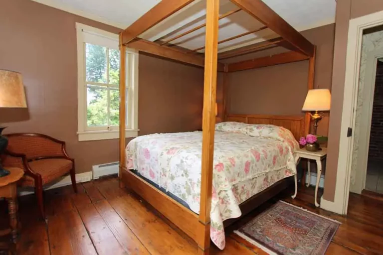 Bedroom with a four-poster bed, floral bedding, window view, and warm lighting.