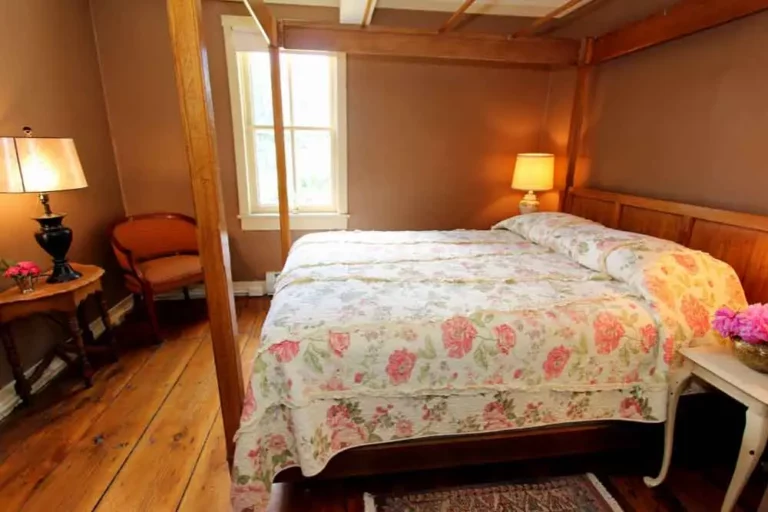 Bedroom with a floral-patterned bedspread, wooden furniture, and natural light from window.