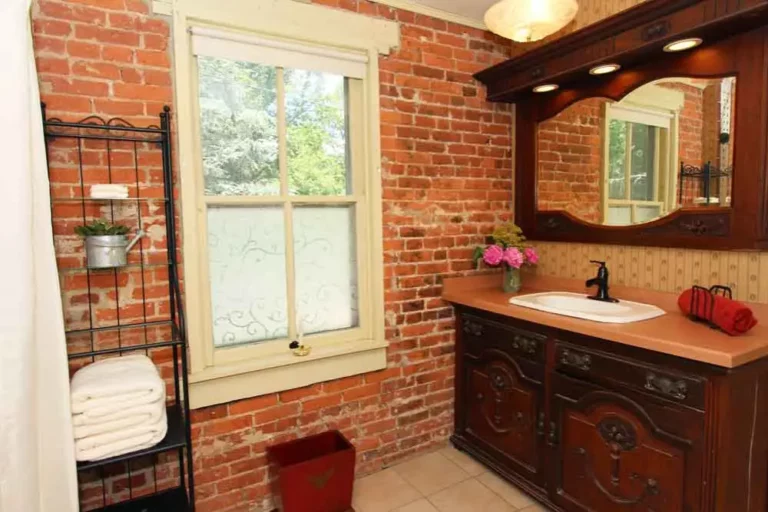 Bathroom with exposed brick walls, wooden vanity, and a window overlooking greenery.