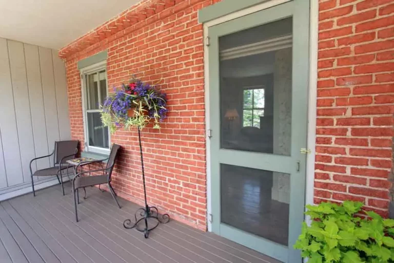 Screen door and hanging flower basket on brick porch wall