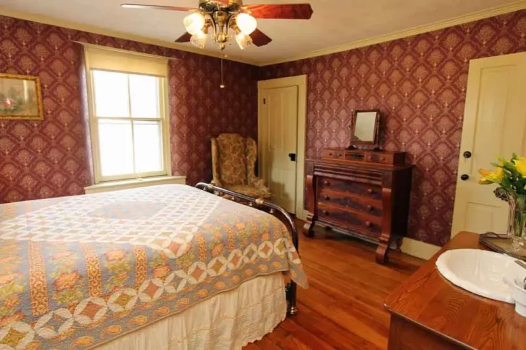 Bedroom with patterned wallpaper and antique dresser.