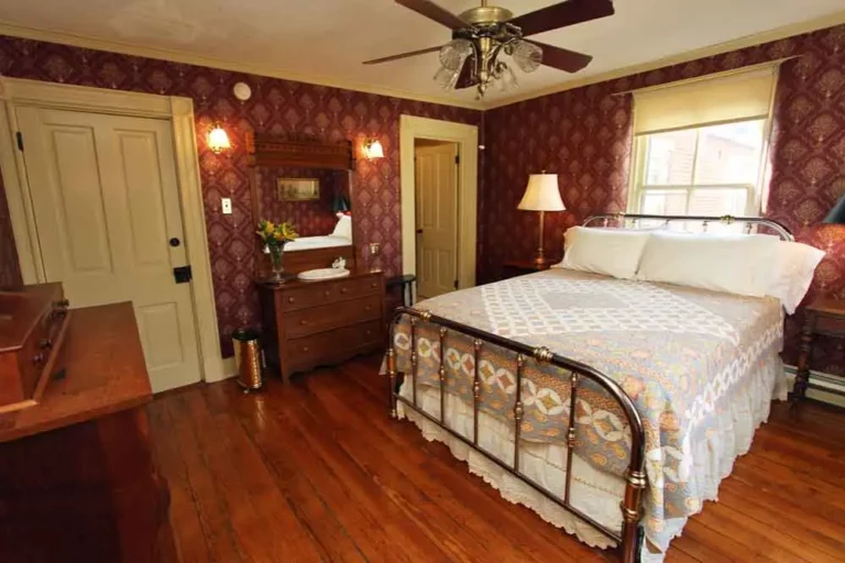 Bedroom with patterned wallpaper and antique dresser.