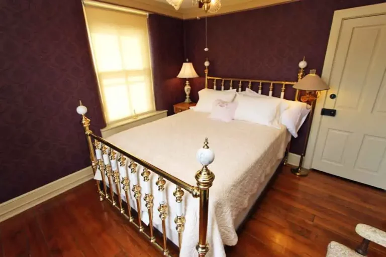 Elegant bedroom with a large brass bed, white bedding, purple walls, and two bedside lamps.